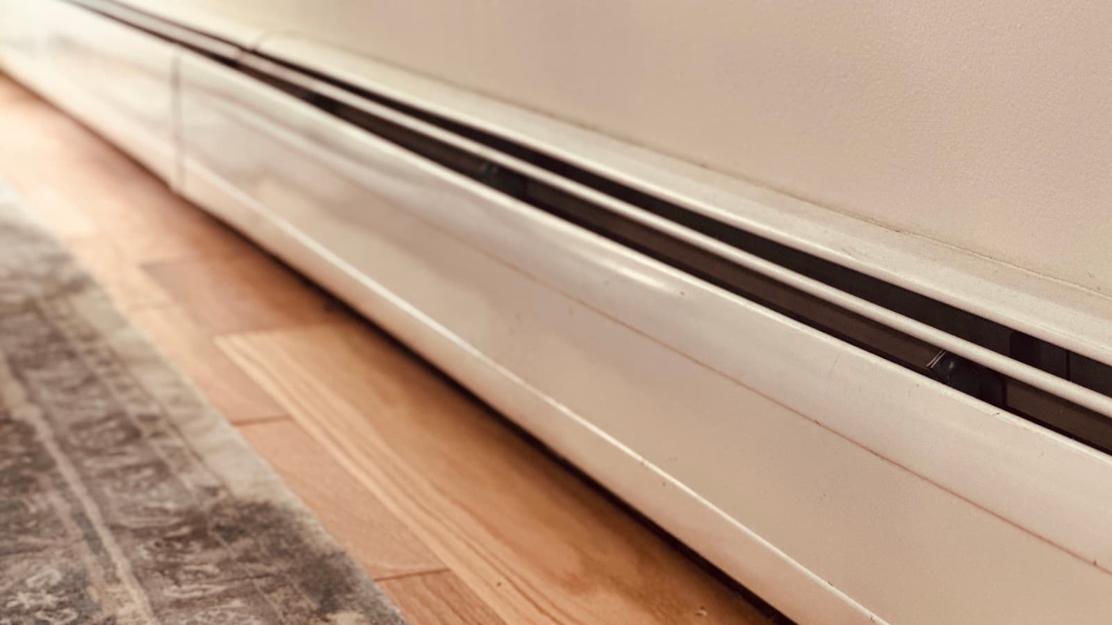 Hydronic fin-tube baseboard heater along a wood floor in a Long Island home